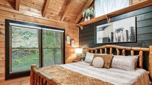 Een slaapkamer in een houten hutje, met een bed, houten hoofdeinde en een raam met zonwering.