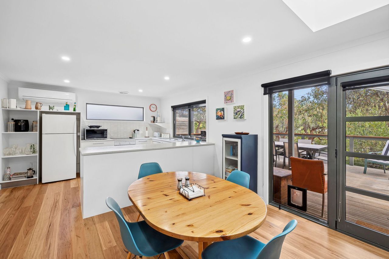 A modern kitchen with a central island, a dining area with a wooden table, and a view of an outdoor deck.
