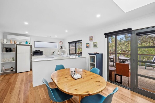 A modern kitchen with a central island, a dining area with a wooden table, and a view of an outdoor deck.