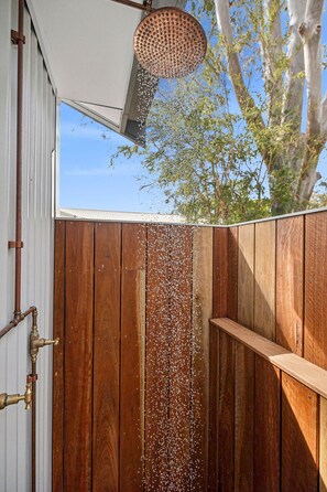 A wooden fence with a showerhead above it, a metal pipe, and a tree in the background.