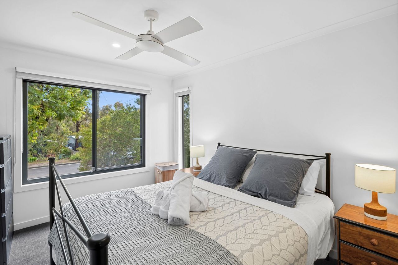 Une chambre à coucher comprenant un lit, des tables de chevet, un ventilateur de plafond et une grande fenêtre donnant sur un paysage verdoyant.