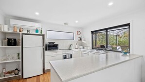 A modern kitchen with white cabinetry, a large island, and a window providing a view of the outdoors. - Kanga Beach House (Anglesea)