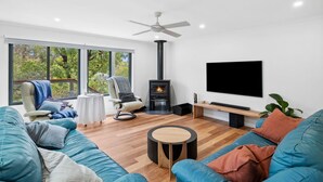 A modern living room with a fireplace, a sofa, a chair, and a TV. - Kanga Beach House (Anglesea)