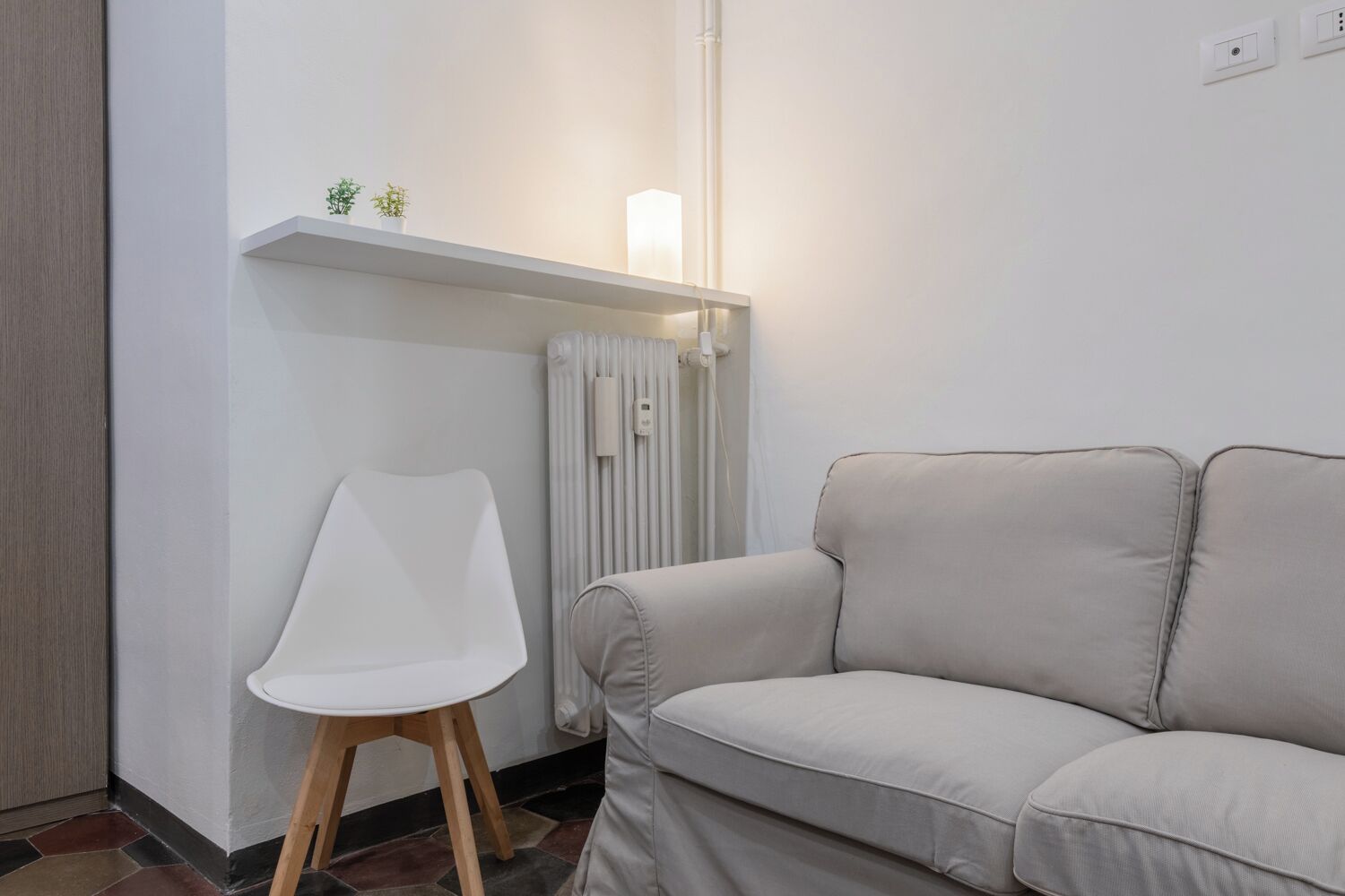 A modern living room with a sofa, a white chair, a radiator, and a shelf with small plants.
