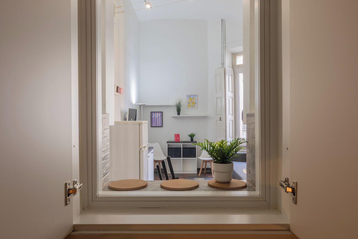A modern interior with a dining area, a refrigerator, and a potted plant.