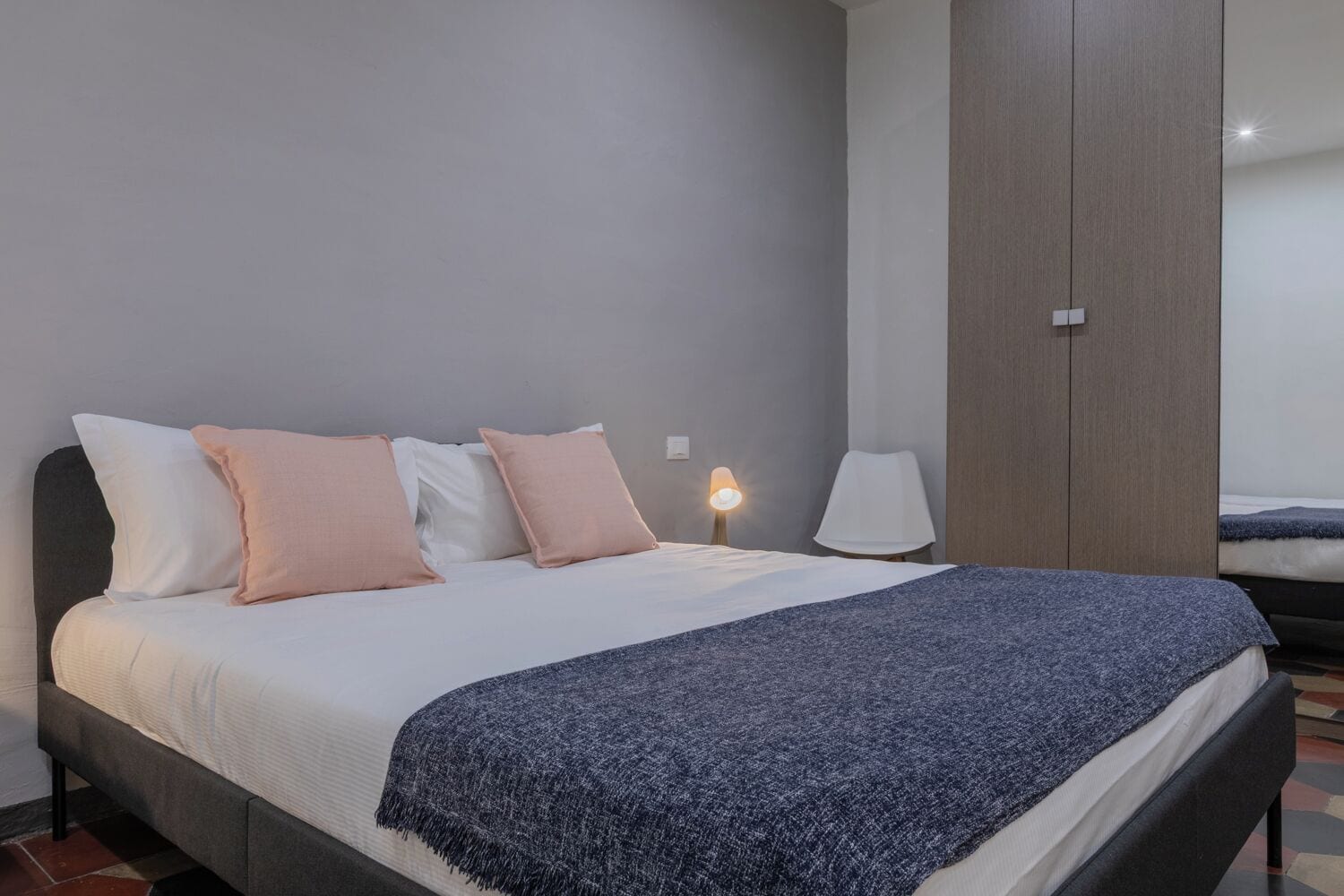 A neatly made bed with a white and blue blanket, two bedside lamps, and a wardrobe in a modern room.
