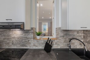 A modern kitchen with a built-in stove, a sink, and a window with a view into the living area. - Conte Verde Apartments by Wonderful Italy (Turin)