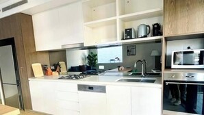A modern kitchen with white cabinetry, a built-in dishwasher, a stainless steel range hood, and a microwave. - Amazing 2 bedrooms condo [Street Parking, WiFi] (Zetland)
