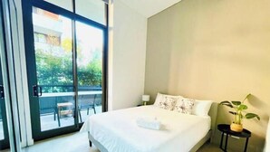 Ein Hotelzimmer mit einem großen Bett, einem kleinen Nachttisch, einer Topfpflanze und einer Glastür, die zu einem Außenbereich führt.