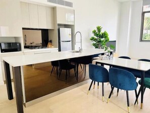 A modern kitchen with white cabinetry, a central island, and a dining area with blue chairs. - Charming and cozy 3 Bedroom Condo [Parking, Wi-Fi] (Roseville)