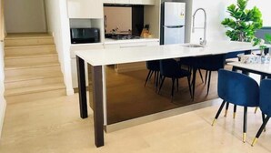 Eine moderne Küche mit einer zentralen Kochinsel, dunklen Stühlen und einer weißen Arbeitsplatte.