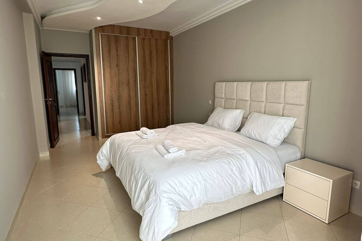 A bedroom with a large bed, a wooden wardrobe, and a nightstand.