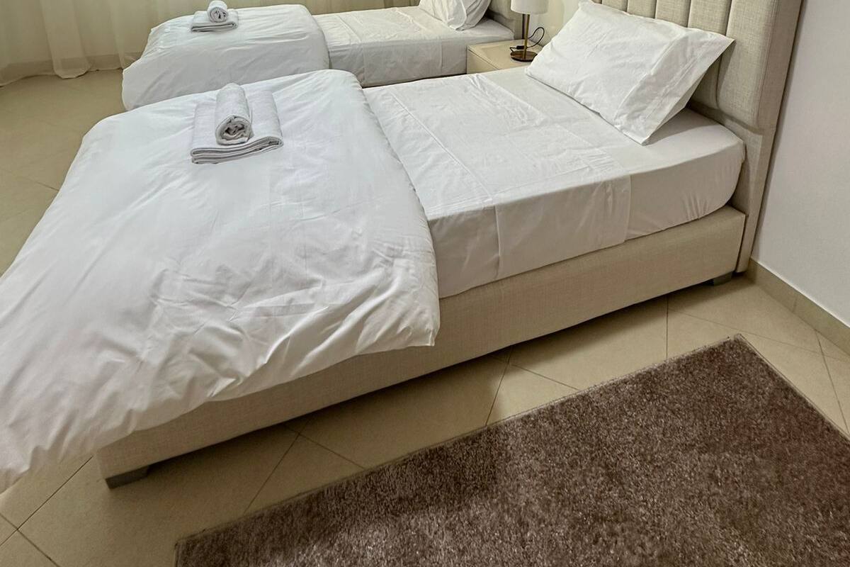 A hotel room with two beds, a large window with sheer curtains, a brown rug, and a decorative wall molding.