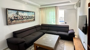 A modern living room with a large sectional sofa, a coffee table, and a painting on the wall. - SHRTSTAYS Guesthouse (Tangier)