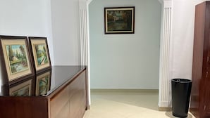 A hallway with a wooden reception desk, framed pictures, a painting on the wall, and a trash can. - SHRTSTAYS Guesthouse (Tangier)