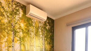 Un dormitorio con cama, ventana, aire acondicionado y un mural de un bosque en la pared.