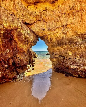 A natural rock formation with a cave entrance leading to a beach.