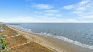 A beach with a pier extending into the ocean, a sandy shore, and a clear sky.
