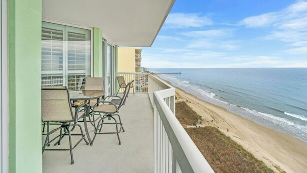 A balcony with outdoor furniture overlooking a beach and ocean.