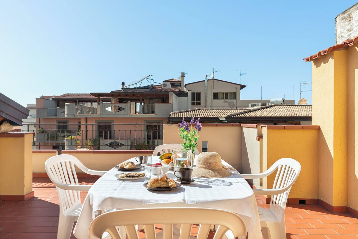 Een terras met een ontbijttafel, compleet met croissants, fruit en een vaas met bloemen.