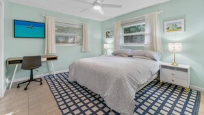 Ein Schlafzimmer mit einem Bett, einem Schreibtisch, einem Stuhl, einem Nachttisch, einer Lampe und einem Deckenventilator.