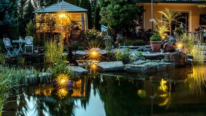 A serene garden with a pond, a gazebo, and a patio area with outdoor furniture. - Glückliche Kuh-Villa (Kempten)