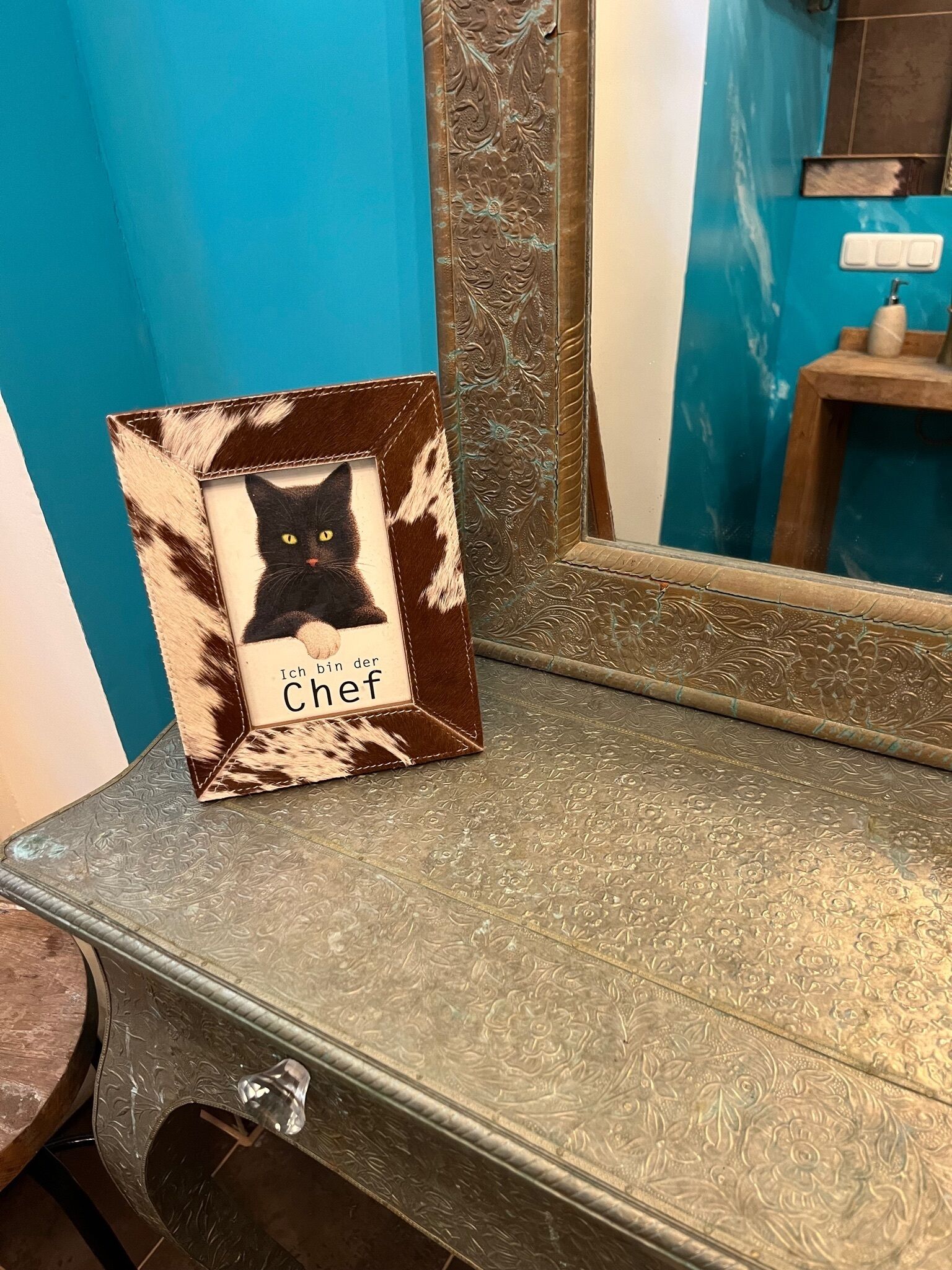A bathroom vanity with a mirror, a framed picture of a cat, and a towel rack.