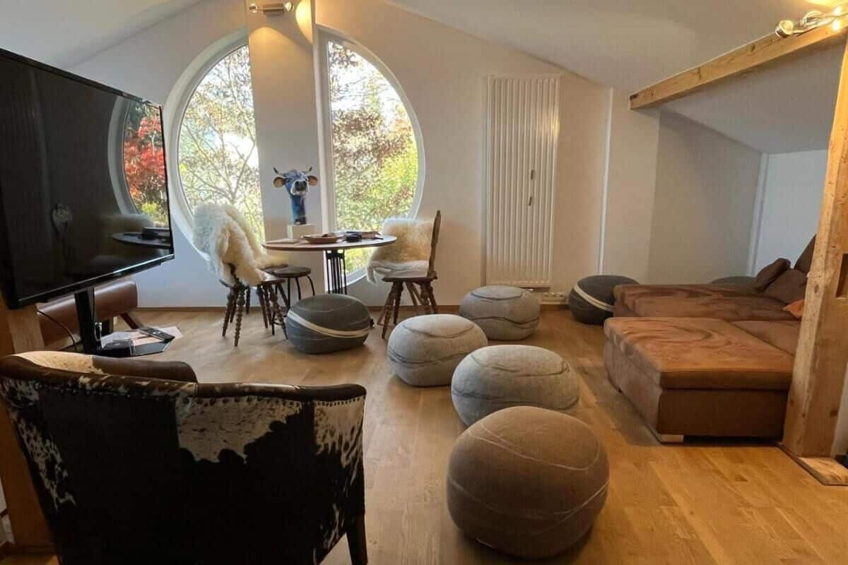 Uma sala de estar moderna com televisão de tela plana, pufes redondos, um sofá e um espaço de jantar com cadeiras e uma mesa.