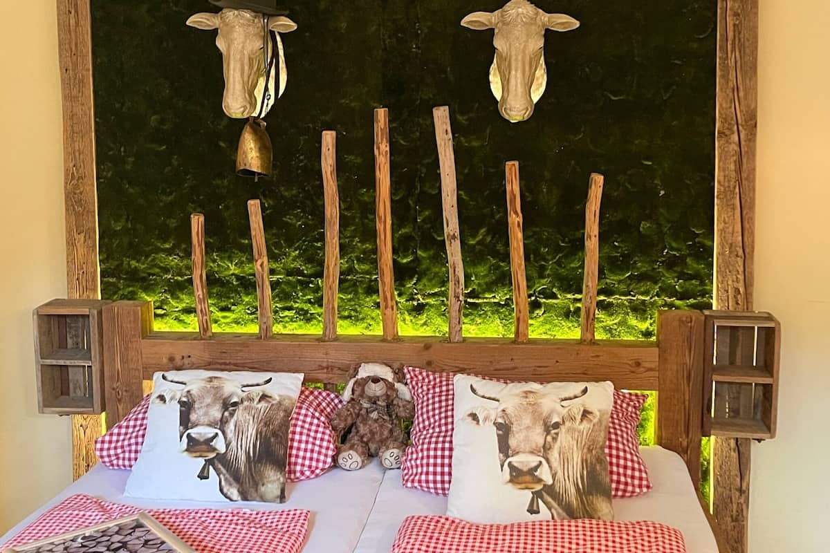 Cama com cabeceira de madeira, decorada com almofadas de vaca e cabeça de vaca pendurada acima.