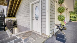 A house with a stone staircase leading to a white door with an oval glass window. There is a small garden with a potted plant and an American flag.