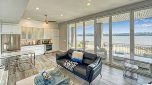 A spacious living area with a large window overlooking a lake, a modern kitchen, and a balcony with outdoor seating.