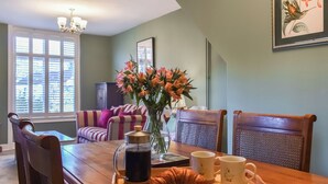 A dining area with a wooden table, chairs, a tray with a croissant, coffee, and mugs, a vase with flowers, and a framed picture on the wall. - 2 bedroom accommodation in Sinnington near Pickering (Sinnington near Pickering)
