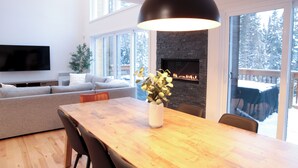 A modern living room with a large TV, a fireplace, and a dining area with a wooden table and chairs.