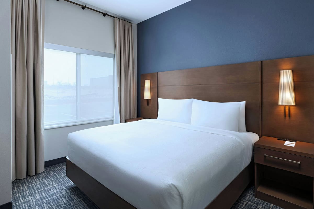 Una habitación de hotel con una cama grande, una mesita de noche, una lámpara y una ventana con cortinas.