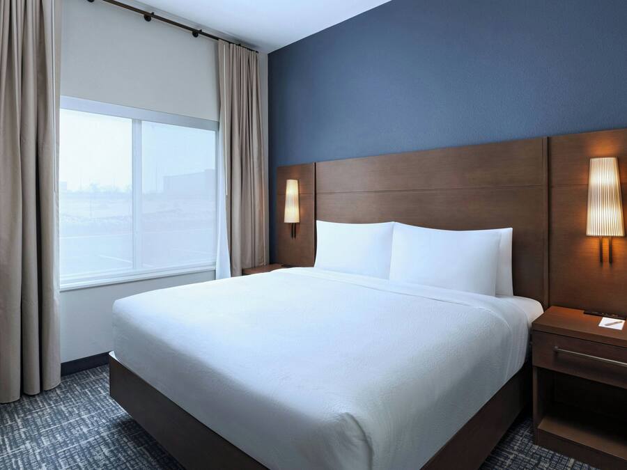 Una habitación de hotel con una cama grande, una mesita de noche, una lámpara y una ventana con cortinas.