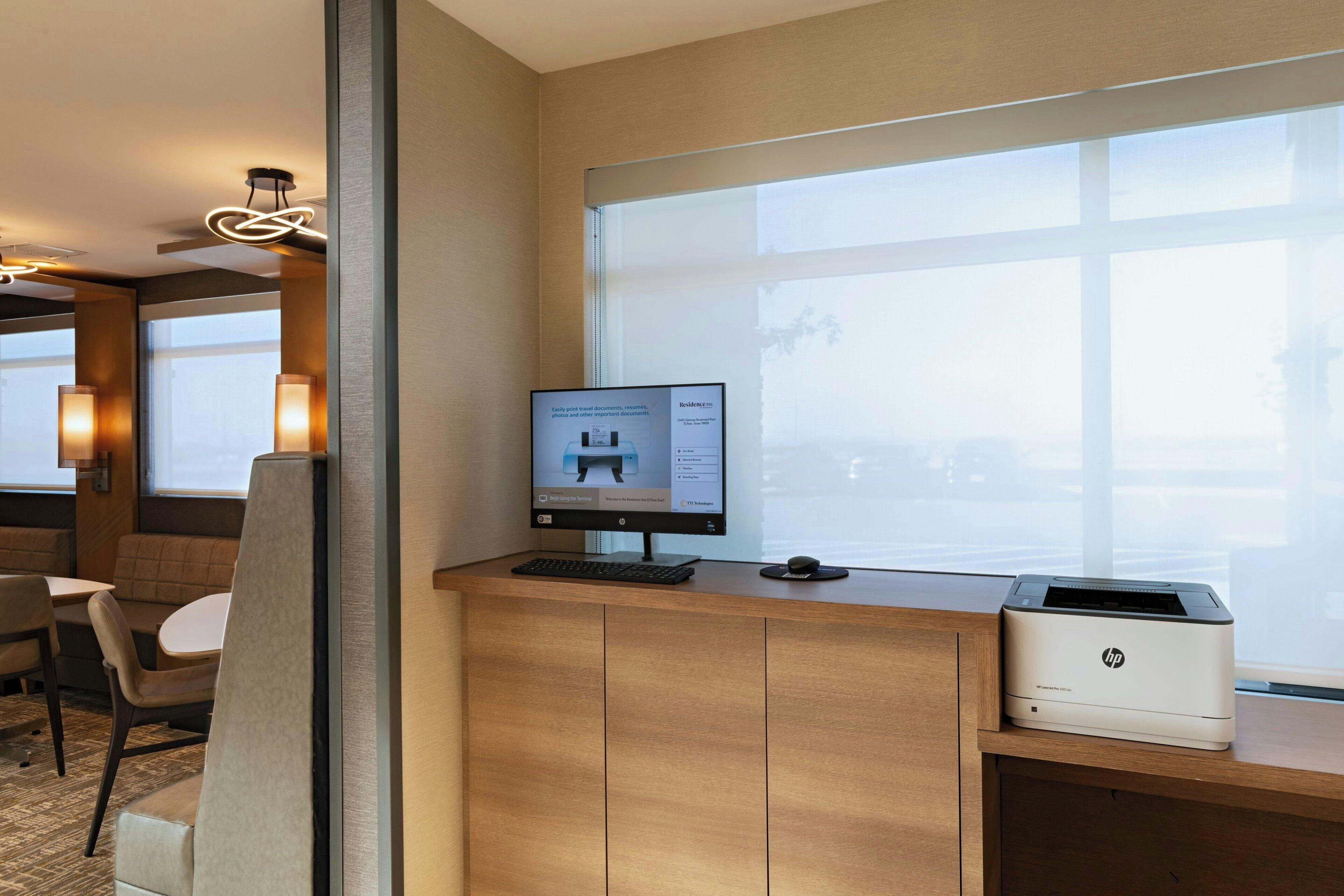 A hotel reception desk with a computer monitor, HP printer, and seating area.