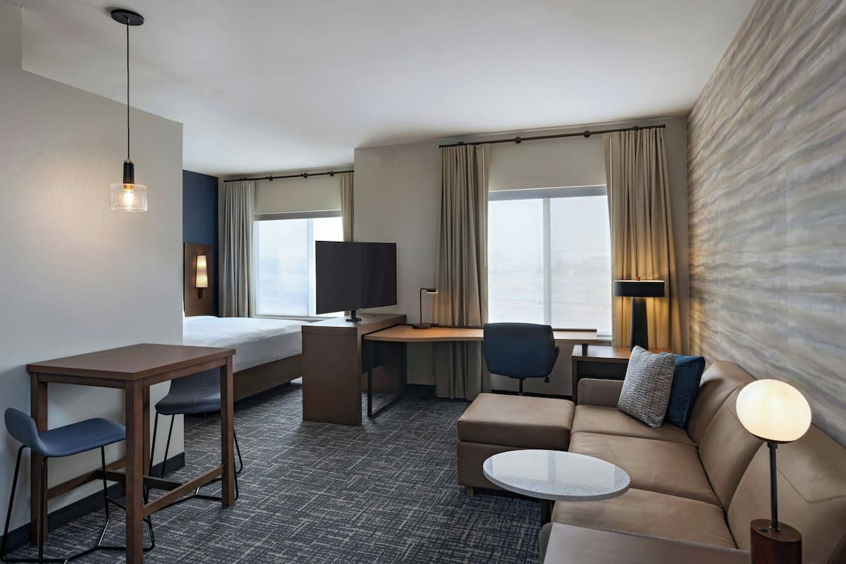 Una habitación de hotel con cama, escritorio, sofá, una mesita y televisor.