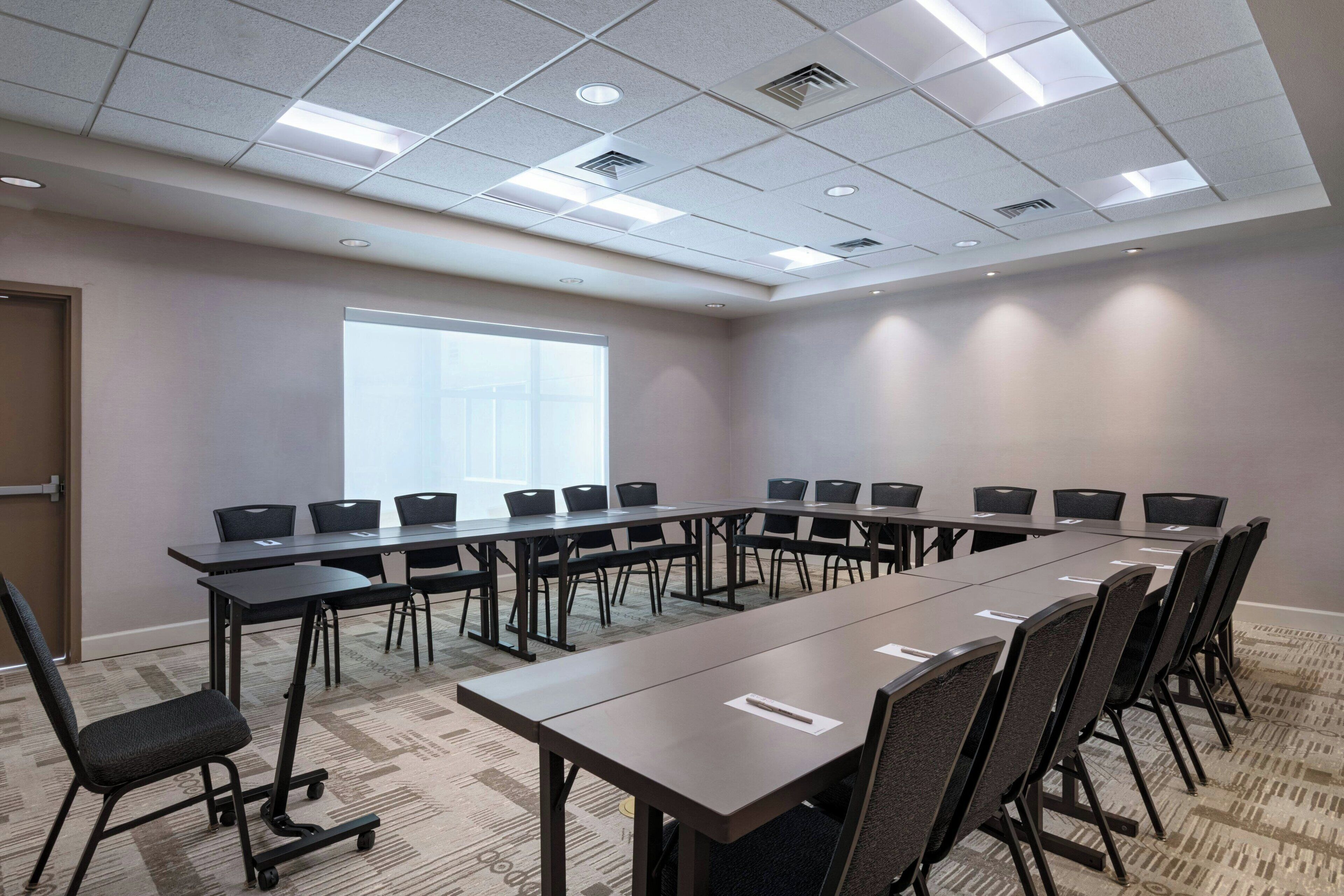 A conference room with a long table, chairs, a projector screen, and a carpeted floor.