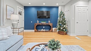 Ein Wohnzimmer mit blauer Akzentwand, einem an einer Holzkonsole montierten Flachbildfernseher, einem Weihnachtsbaum und einem grauen Sofa.