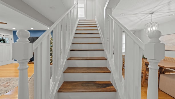 Eine Treppe mit weißen Geländern und Holzdielen, die zu einer Zwischenebene im zweiten Stock führt.