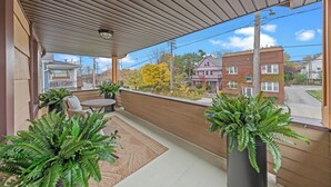 Ein überdachter Balkon mit Sitzgelegenheit, Topfpflanzen und Blick auf umliegende Gebäude.