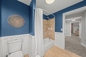 Un baño con inodoro blanco, ducha con cortina blanca y zona de baño de madera.