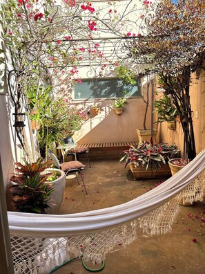 Un patio exterior acogedor con una hamaca, plantas en macetas y un banco de madera.