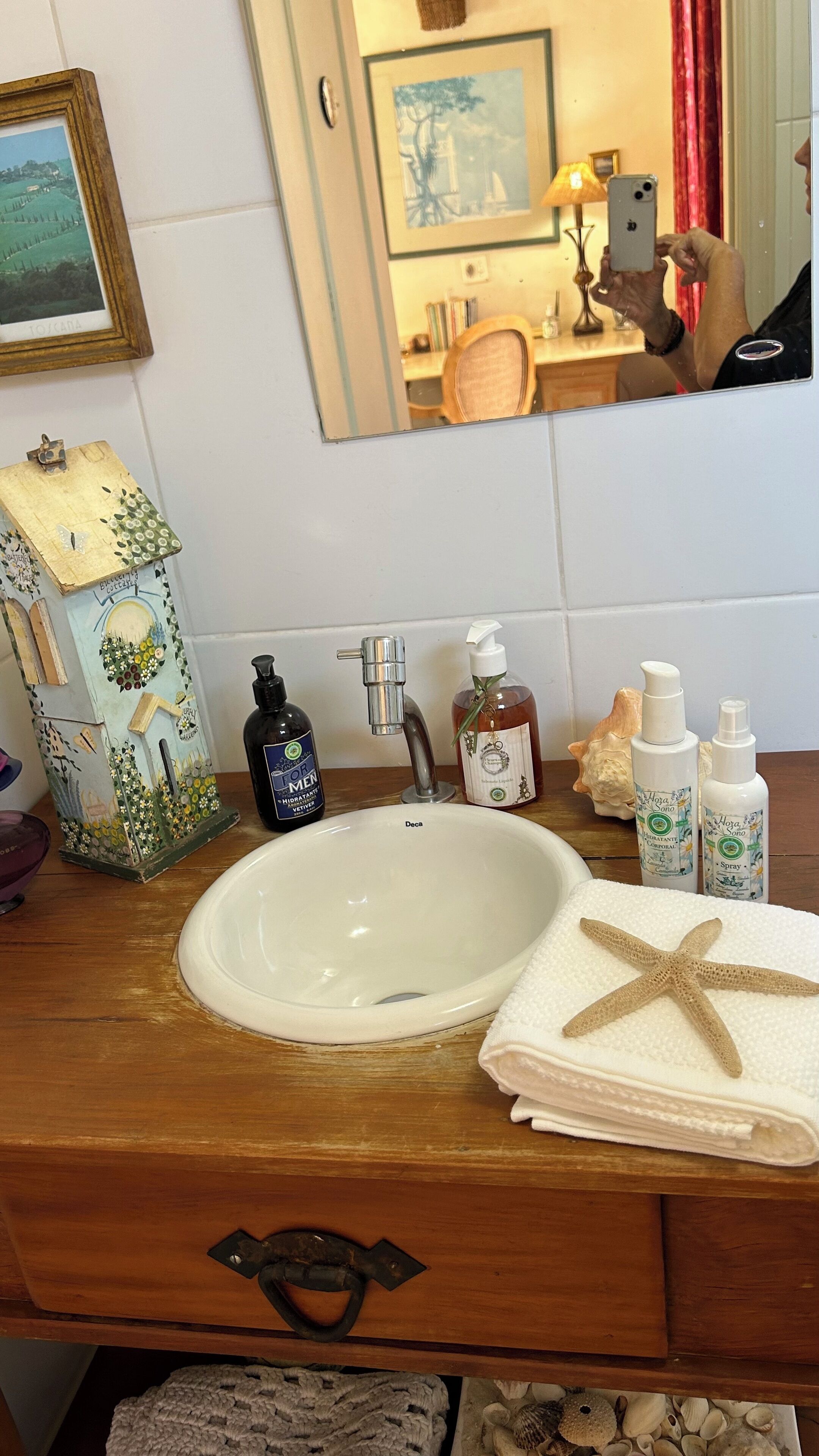 Casa de banho com toucador de madeira, lavatório branco e diversos artigos de higiene pessoal.