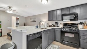 Een moderne keuken met grijze kastjes, een wit aanrecht, een ingebouwde oven, een magnetron en een vaatwasser.