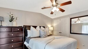 Een slaapkamer met een bed, een dressoir, een plafondventilator en een spiegel.