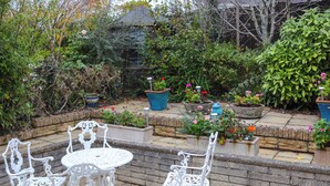 A garden patio with white metal chairs and a table, surrounded by stone walls and potted plants. - Berllys Annex - UK48482 (Criccieth)