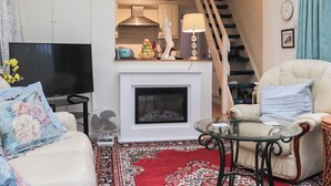 A living room with a fireplace, a television, a sofa, a glass coffee table, and a staircase leading to a kitchen. - Berllys Annex - UK48482 (Criccieth)
