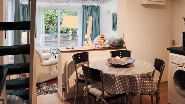 A dining area with a round table, chairs, a washing machine, and a window with curtains. - Berllys Annex - UK48482 (Criccieth)