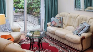 A living room with a sofa, a glass coffee table, a red rug, and a view of greenery through a sliding door. - Berllys Annex - UK48482 (Criccieth)